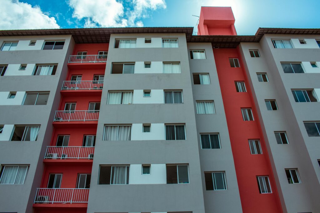 A high-rise residential building featuring a striking red facade and balconies against a blue sky.
