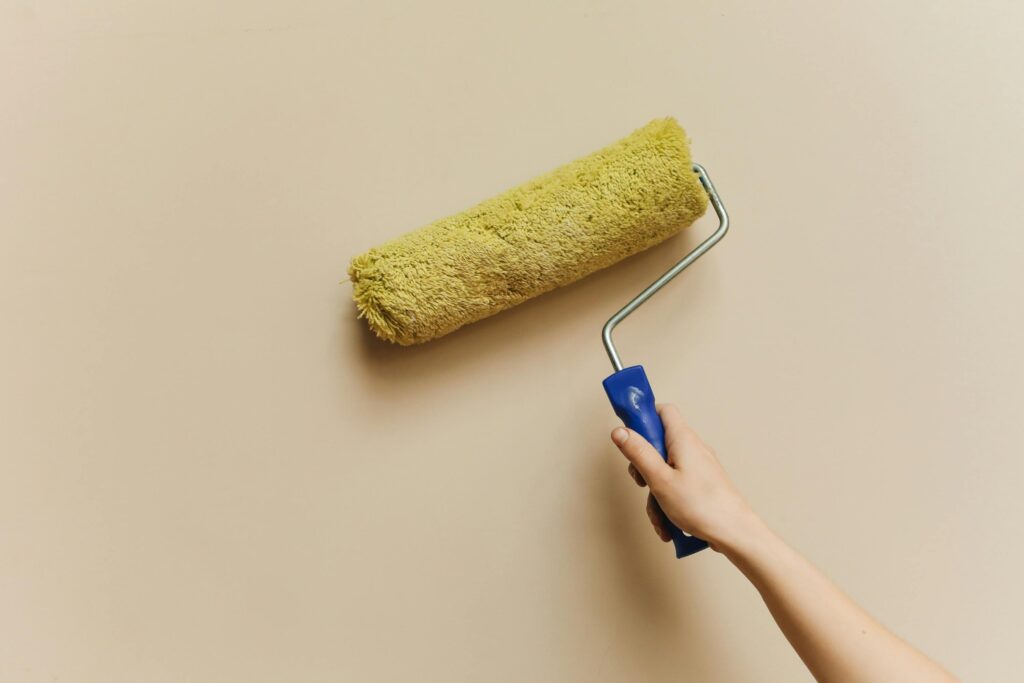 A hand using a yellow paint roller to paint a beige wall. Perfect for DIY and home improvement themes.