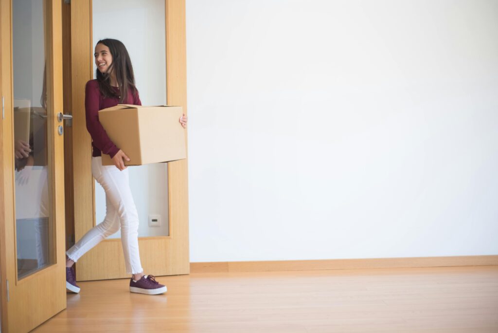 A woman enters a new apartment carrying a cardboard box, symbolizing moving in.